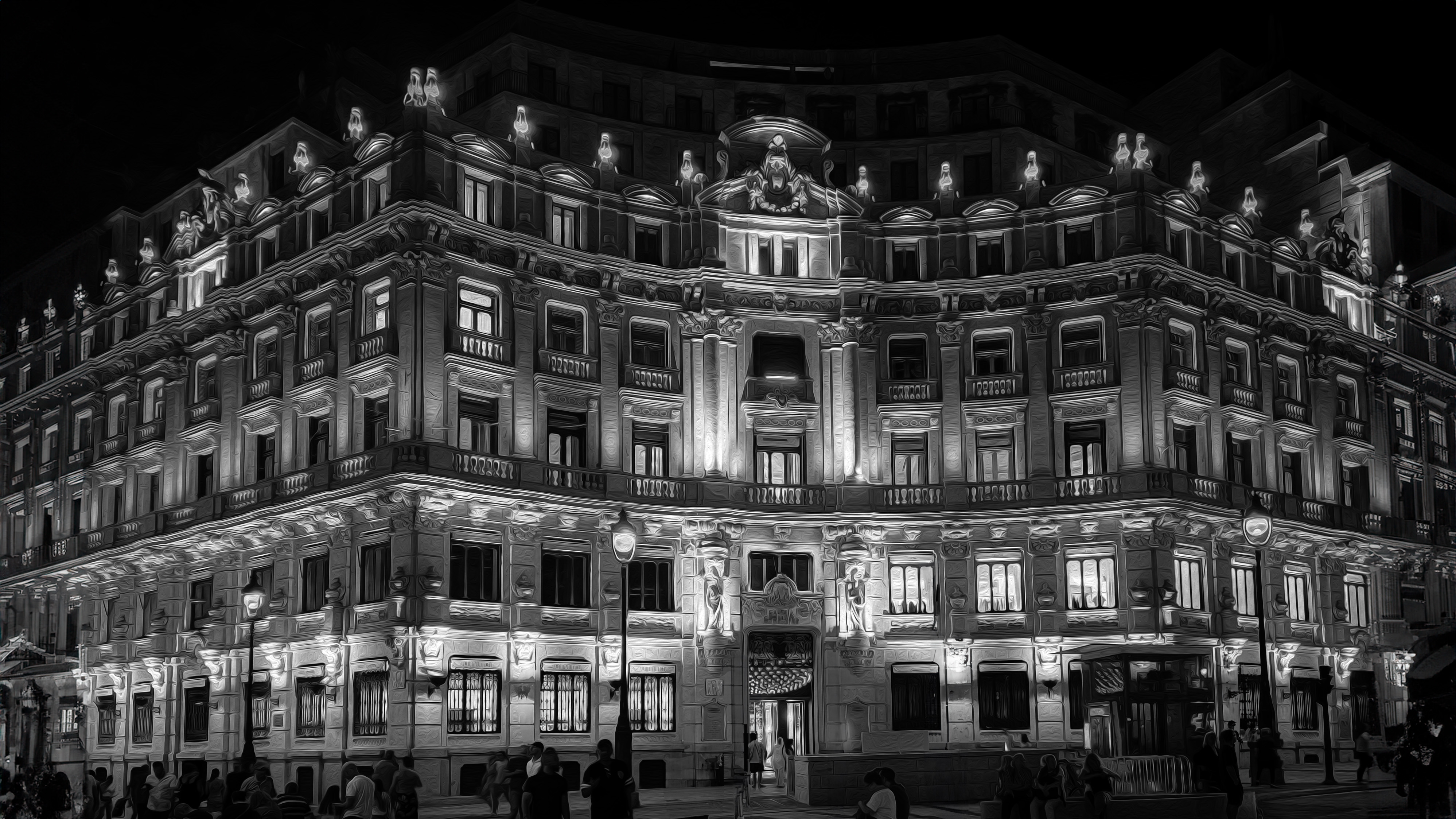 A black-and-white image of a beautifully lit historic building in Madrid, Spain, with intricate architectural details and glowing lights.