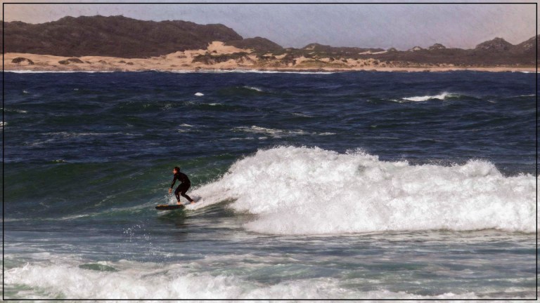 Surfer balancing on a wave under overcast skies near a sandy South African shoreline
