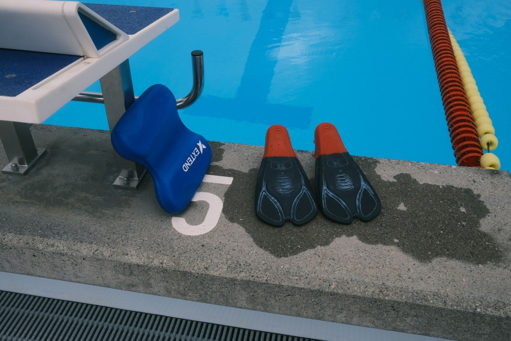 Swimming fins and a kickboard beside a pool lane — symbolizing small beginnings, movement, and personal growth in gentle waters.