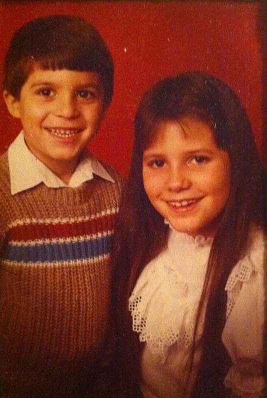 Childhood portrait of my two children, a smiling young boy and girl, photographed together against a warm red background.