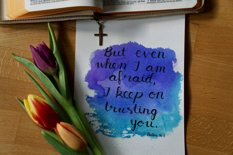 Open Bible, cross necklace, tulips, and watercolor Scripture card reading, “But even when I am afraid, I keep on trusting you.”