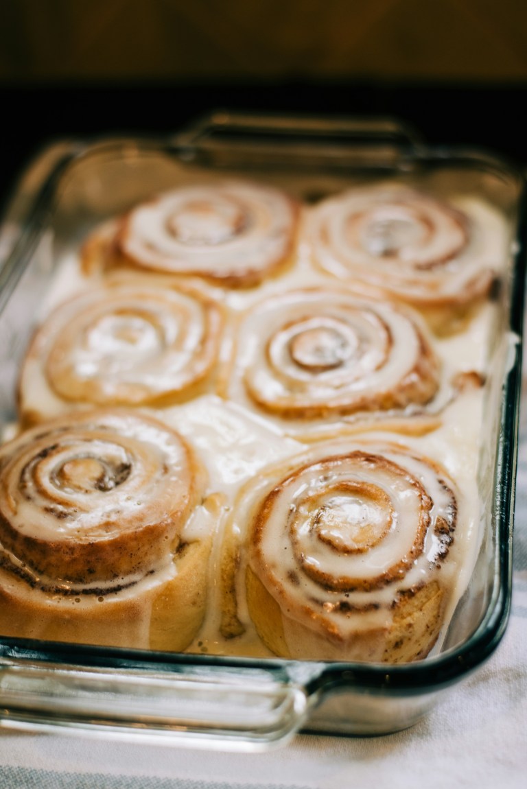 Freshly baked cinnamon rolls covered with creamy icing in a glass baking dish.